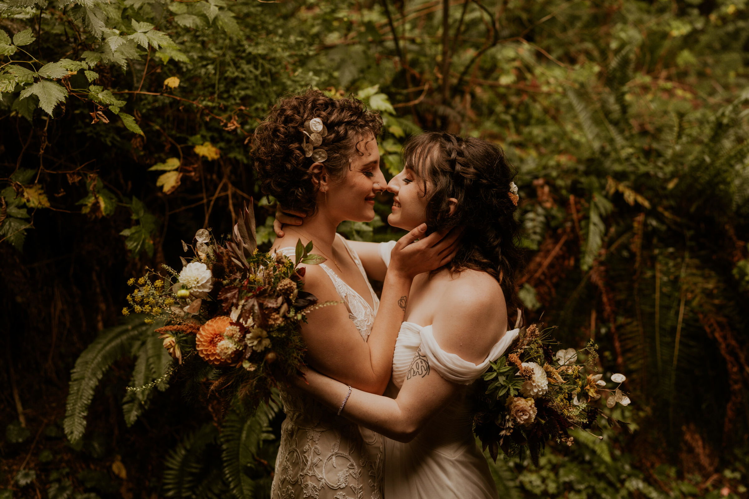 Two brides hold each other in a forest.